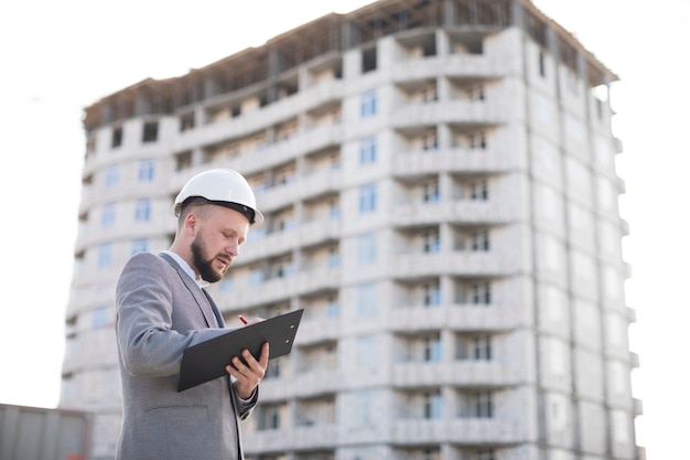 Escritura masculina joven de la arquitectura en el tablero en el emplazamiento de la obra