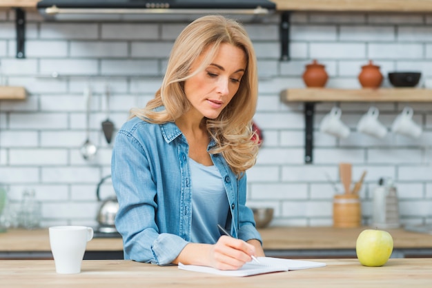 Foto gratuita escritura rubia de la mujer joven con la pluma en el cuaderno sobre la tabla de madera