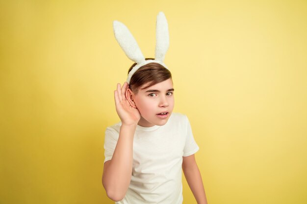 Escuche el secreto. Muchacho caucásico como un conejito de Pascua en el fondo amarillo del estudio. Felices saludos de pascua. Hermoso modelo masculino. Concepto de emociones humanas, expresión facial, vacaciones. Copyspace.