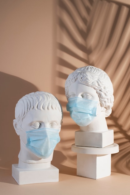 Esculturas de mármol de figuras históricas con máscaras médicas y sombra de hojas.