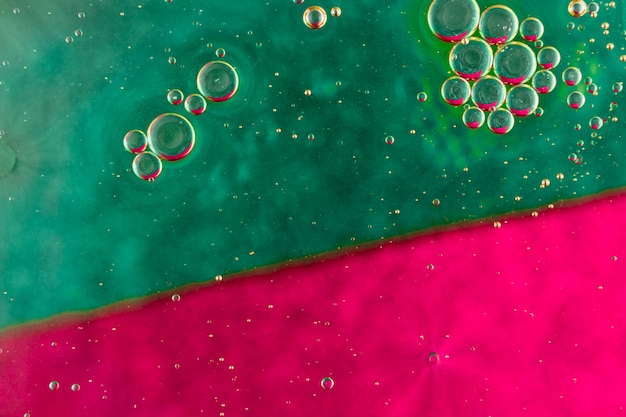 Esfera en forma de burbujas de aceite flotando en la superficie del agua de color verde y rojo