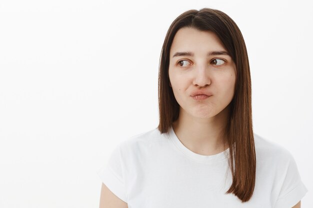 Eso apesta. Mujer disgustada y decepcionada, malestar de planes arruinados, sonriendo con sus labios doblados en arrepentimiento y consternación, mirando a la izquierda insatisfecha con irritación y molestia por la pared gris