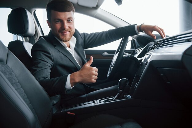 Eso es genial. Hombre de negocios moderno probando su nuevo coche en el salón del automóvil