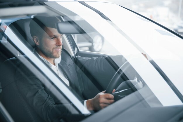 Eso es lo que parece el éxito. Hombre de negocios moderno probando su nuevo coche en el salón del automóvil