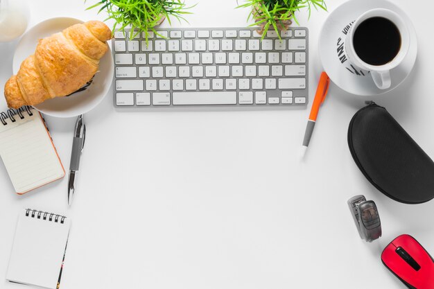 Espacio de trabajo blanco con papelería de oficina y desayuno.