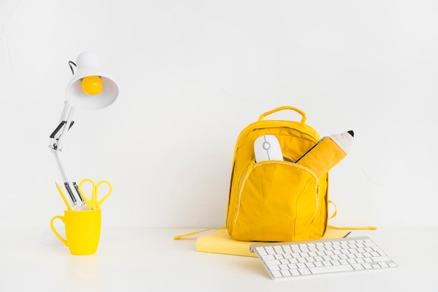 Espacio de trabajo brillante con mochila amarilla y teclado