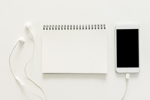 Espacio de trabajo mínimo - Foto plana creativa de escritorio de espacio de trabajo con cuaderno de bocetos y teléfono móvil con pantalla en blanco sobre fondo blanco de espacio de copia. Vista superior, fotografía plana.