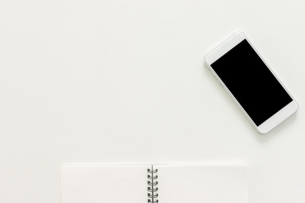 Espacio de trabajo mínimo - Foto plana creativa de escritorio de espacio de trabajo con cuaderno de bocetos y teléfono móvil con pantalla en blanco sobre fondo blanco de espacio de copia. Vista superior, fotografía plana.