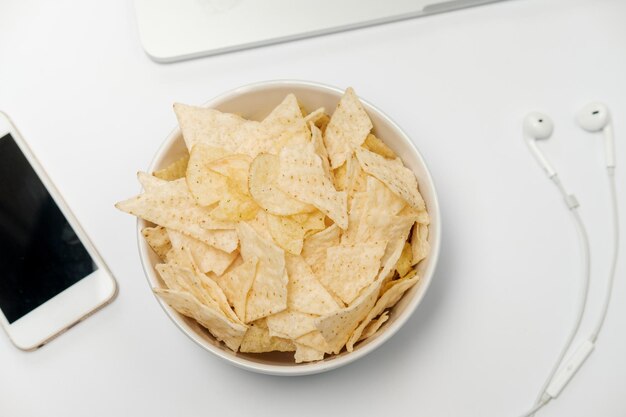 Espacio de trabajo con papelería de papel arrugado portátil y chips en la mesa blanca Concepto de malos hábitos