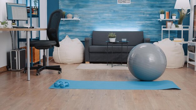 Espacio vacío con material de entrenamiento para entrenar en casa. Nadie en salón con tapete, mancuernas y pelota tonificadora para hacer ejercicio físico y practicar deporte. Fitness y gimnasia