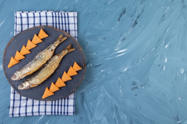 Foto gratuita espadín salado seco y chips de cono en una tabla sobre una toalla, sobre el fondo de mármol.