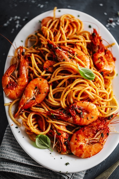 Espagueti de pasta con camarones y salsa de tomate servido en plato sobre superficie oscura. De cerca.