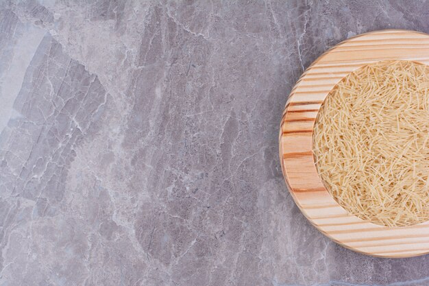 Espaguetis de arroz en bandeja de madera sobre el mármol.