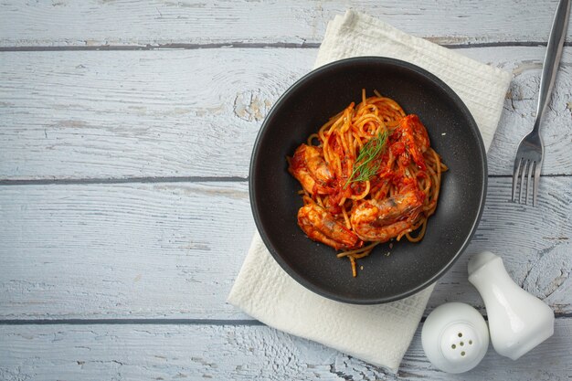 Espaguetis con camarones en salsa de tomate sobre fondo de madera blanca