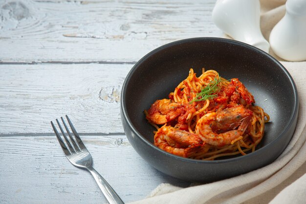 Espaguetis con camarones en salsa de tomate sobre fondo de madera blanca