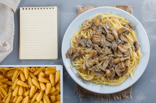 Espaguetis y champiñones con cuaderno, pasta cruda, papel de cocina en un plato