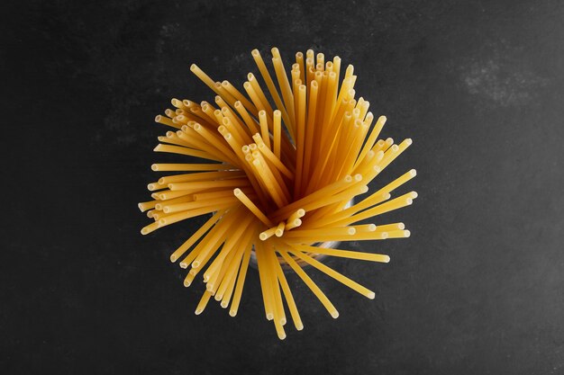 Espaguetis crudos en el centro sobre superficie negra.