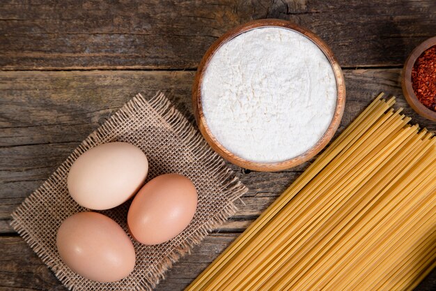 Espaguetis crudos, huevos y tazón de pimienta en grano colocados sobre la superficie de madera. Foto de alta calidad