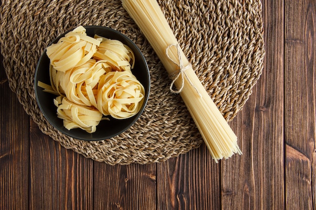 Espaguetis crudos con pasta fettuccine plana sobre fondo de mantel de madera y mimbre