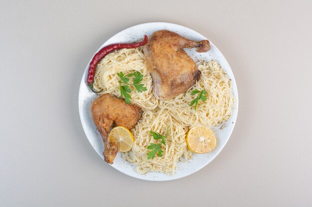 Espaguetis hervidos, pimienta y muslos de pollo en la placa blanca.