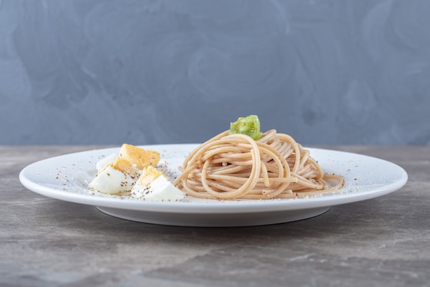 Espaguetis con huevo cocido en un plato blanco.