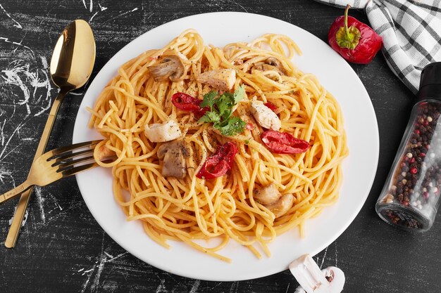 Espaguetis con ingredientes mixtos en un plato blanco con cubiertos reservados.
