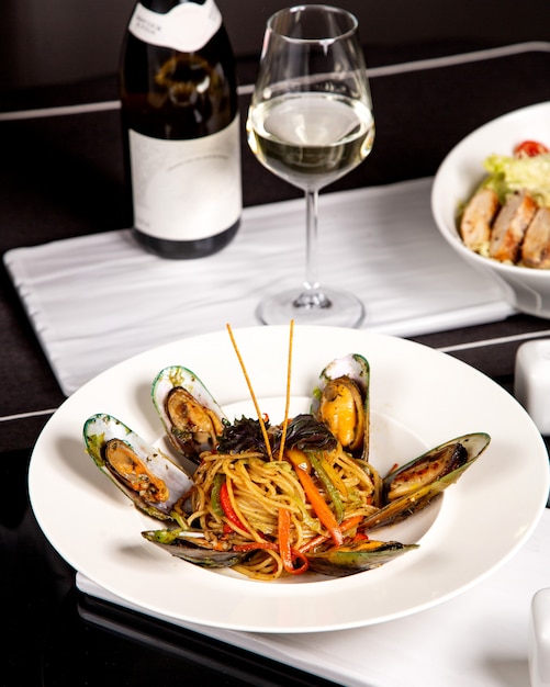 Espaguetis con mejillones y pimientos servidos con vino blanco