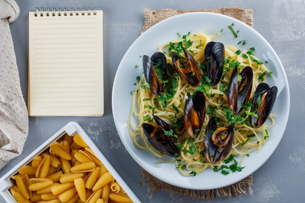 Espaguetis y mejillones en un plato con cuaderno, pasta cruda, papel de cocina