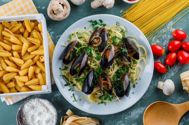 Espaguetis y mejillones en un plato con pasta cruda, tomate, harina, champiñones, cuchara de madera