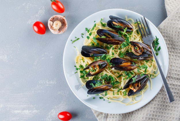 Espaguetis y mejillones con tomate, champiñones, tenedor en un plato sobre papel de cocina