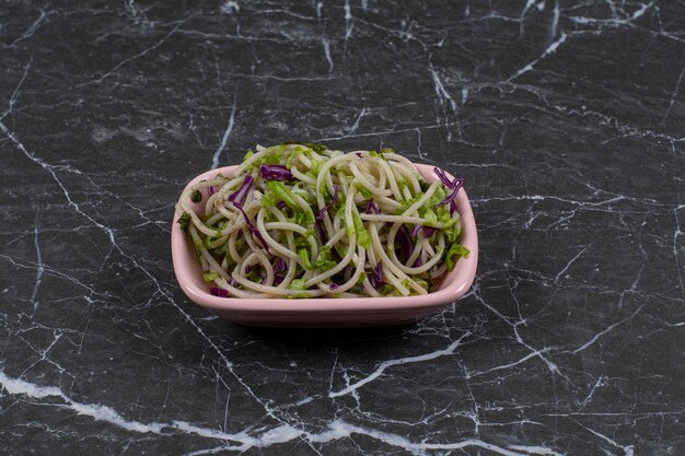 Espaguetis recién hechos con salsa de verduras en un tazón rosa.