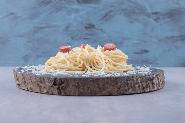 Espaguetis con salchichas fritas sobre pieza de madera.