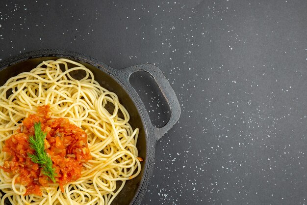 Espaguetis con salsa en la mitad superior de la vista en una sartén en el espacio libre de la mesa negra