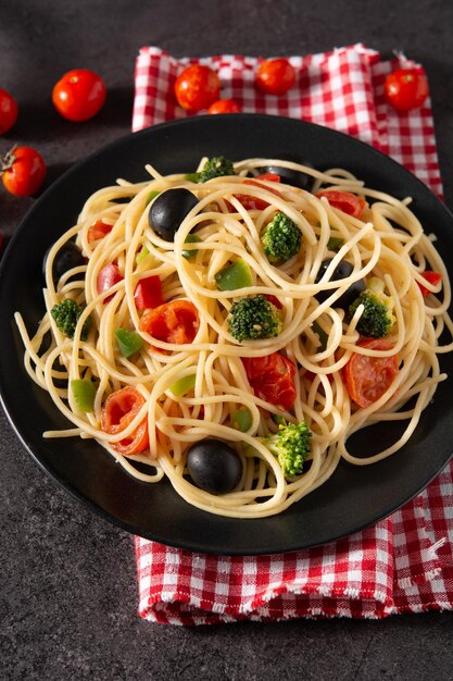 Espaguetis con verduras brócolito tomate pimientos sobre fondo de pizarra negra