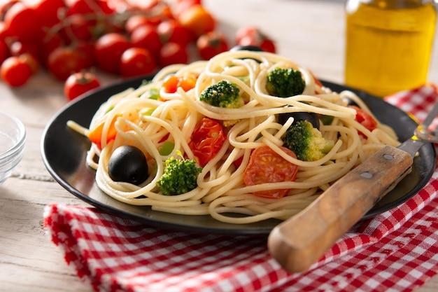 Espaguetis con verduras brócolito tomate pimientos sobre mesa de madera