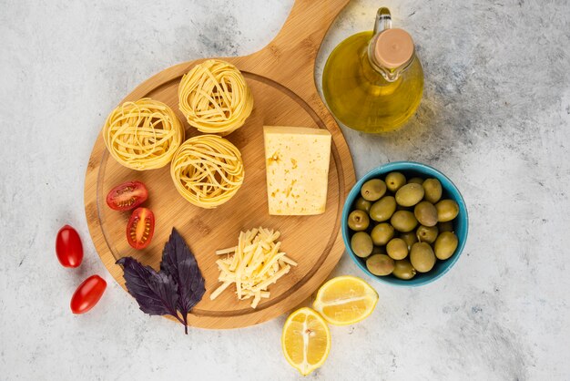 Espaguetis, verduras y queso sobre tabla de madera con aceitunas.