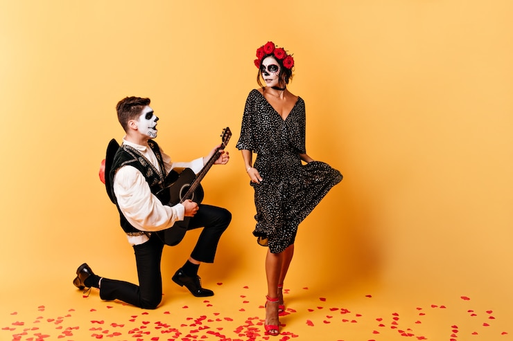 Foto gratuito español en traje nacional canta su canción favorita. chica emocional con máscara de esqueleto en su rostro bailando en la pared naranja