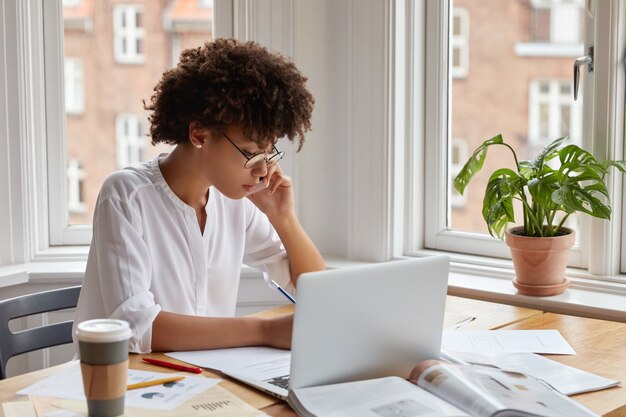 Especialista femenina de piel oscura estudia gráficos, estadísticas, tiene conversación telefónica con un socio comercial