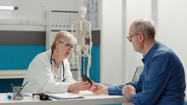 Especialista médico explicando el frasco de medicamentos y pastillas al anciano en el examen de chequeo en el gabinete. Dando tratamiento de prescripción en matraz con analgésicos, drogas y medicamentos.