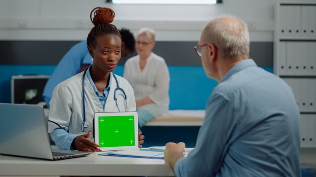 Especialista médico con pantalla verde horizontal en tableta digital en gabinete, analizando antecedentes aislados con paciente mayor. Doctor sosteniendo plantilla de maqueta y tecnología chroma key.