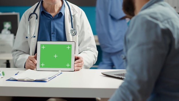 Especialista en salud que muestra una pantalla verde horizontal en una tableta, el paciente mira la pantalla. Plantilla aislada de maqueta con espacio de copia en blanco y fondo de clave de croma en el gadget. De cerca.