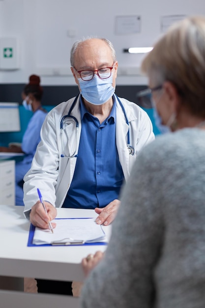 Especialista tomando notas en papeles del portapapeles mientras consulta con una mujer durante la pandemia del covid 19. Médico hombre que prepara el documento de prescripción para el tratamiento contra la enfermedad.