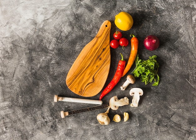 Especias y verduras frescas con tabla de cortar de madera contra el fondo manchado grunge