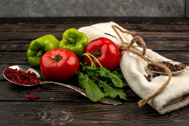 Especias y verduras tomates rojos maduros frescos y pimientos verdes junto con una toalla de color crema en un piso rústico de madera