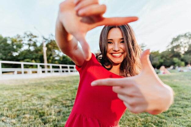 Espectacular chica morena disfrutando de la sesión de fotos de verano. Magnífica dama con expresión de cara feliz jugando en el parque en fin de semana.