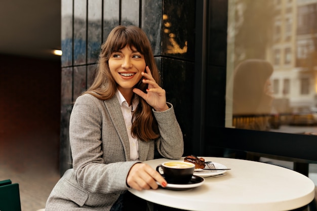 Espectacular mujer con cabello largo oscuro sonriendo durante la pausa para el café.