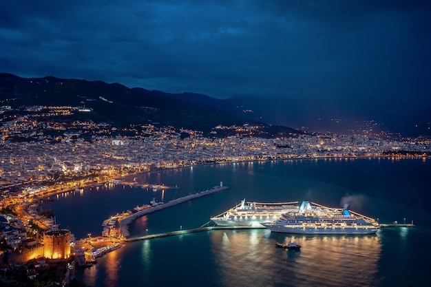 Espectacular noche en la costa del mar con luces de la ciudad y cruceros reflejadas en el agua