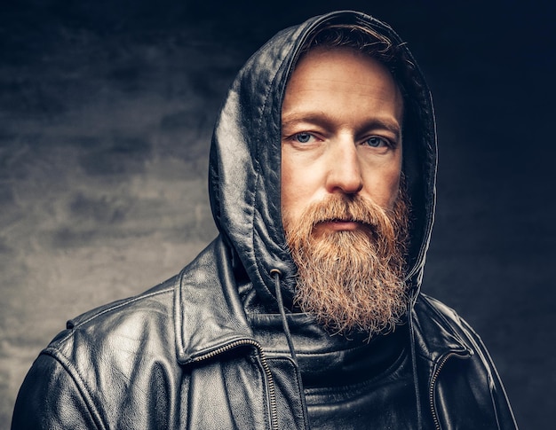 Espectacular retrato de estudio de un hombre barbudo pelirrojo vestido con una chaqueta de cuero sobre un fondo de viñeta gris oscuro.