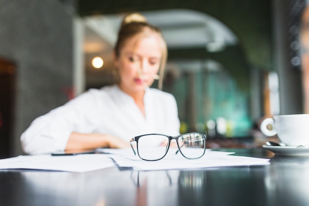 Espectáculos y documento en frente de la mujer de negocios sentado en la cafetería