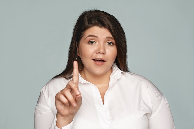 ¡Espera un minuto! Emocional indignada joven mujer de talla grande diciendo No, mostrando el dedo índice, expresando su punto de vista o disentimiento, planteando objeciones, estando totalmente en desacuerdo. Enfoque selectivo